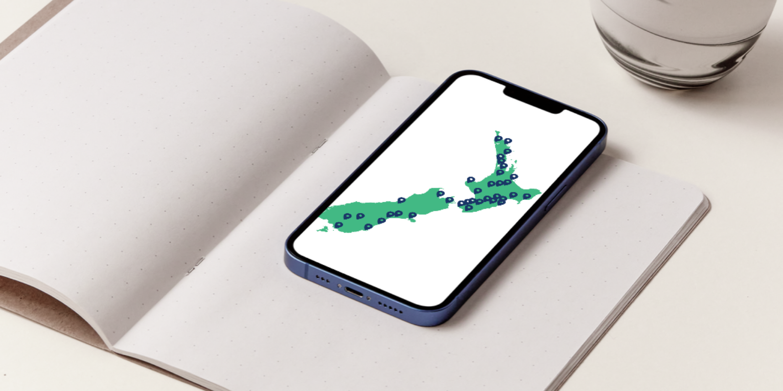 Map of New Zealand with location pins, on a phone on top of an open notebook