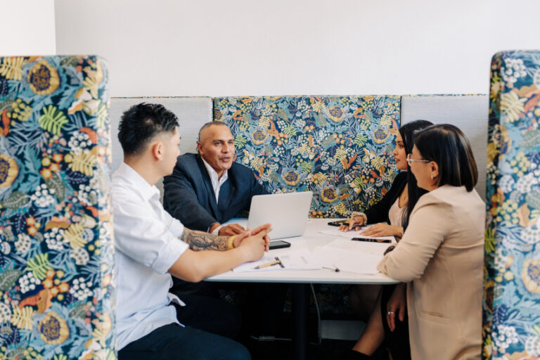 Four adults sitting around the meeting table with a laptop and notes