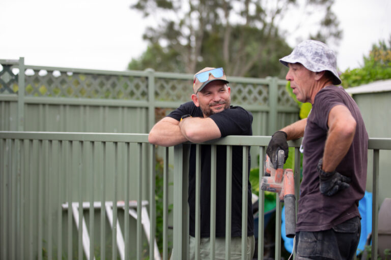 Adult and older adult men talking over a fence
