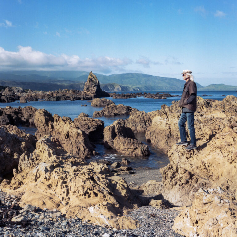 Older adult looking out on the ocean while standing on a rocky beach.