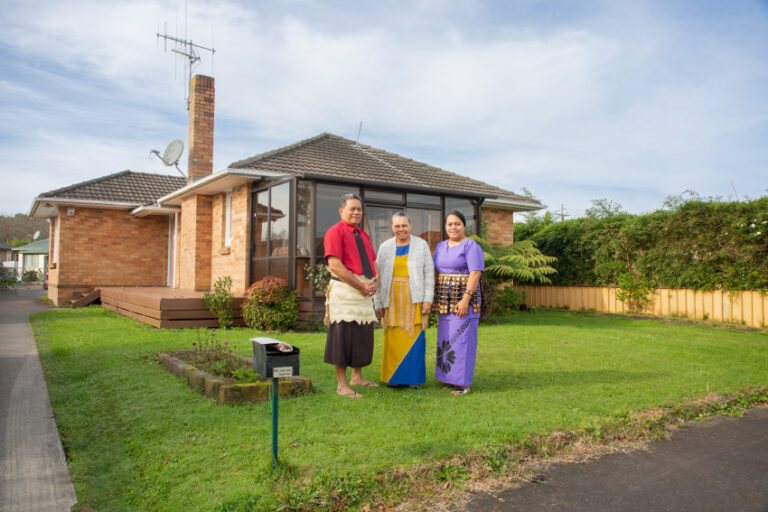 Adult male, older adult woman, and female adult in front of their house