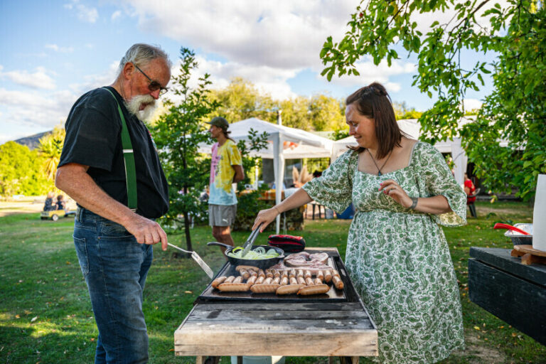 Older adult and woman cooking sausages outdoors