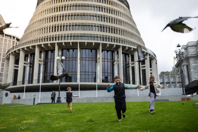 Children running around in the grass with the Parliament in the background
