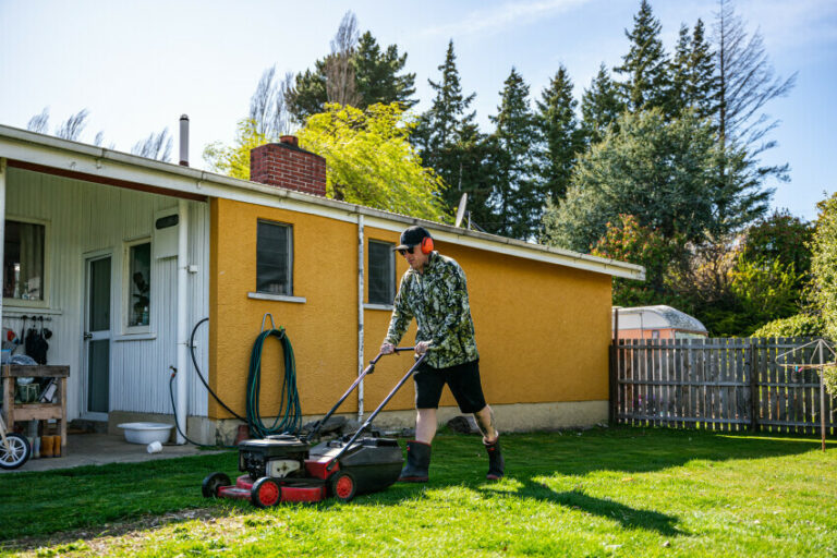 Older adult mowing the lawn with his home in the background